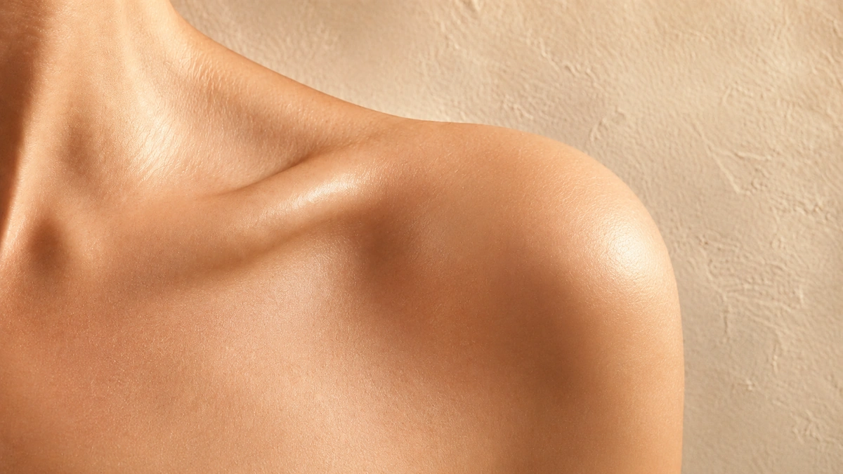 Close-up of naturally hydrated skin across the shoulder and collarbone in warm, soft light.